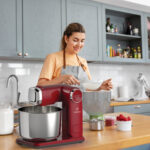 culinary, baking and people concept - happy smiling young woman cooking food on kitchen at home and sifting flour through sieve